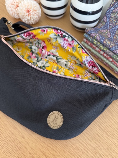 Bolsa preta com forro floral amarelo rodeada por vasos listrados e tecidos estampados