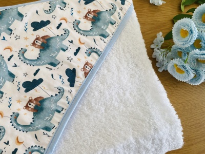Toalha branca com cobertor infantil estampado de dinossauros e ursos, com flores artificiais ao lado