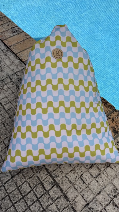Almofada grande com padrão geométrico azul, verde e branco ao lado de piscina