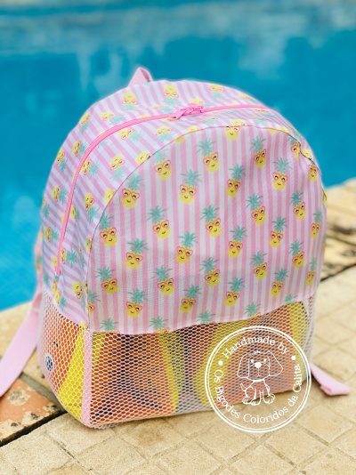 Mochila rosa com padrão de ananases e bolso de rede branco junto à piscina