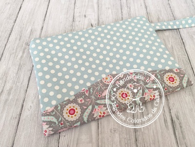 Bolsa ou estojo em tecido azul com bolinhas brancas e padrão floral cinza com alça lateral.