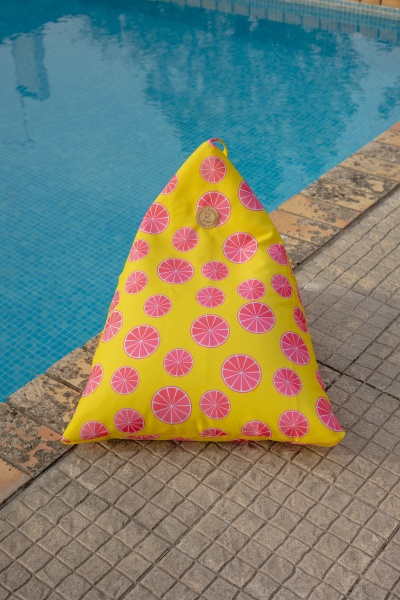 Almofada triangular amarela com fatias de citrinos cor-de-rosa ao lado de uma piscina