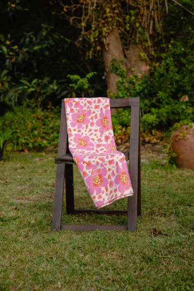 Toalha floral cor de rosa pendurada numa cadeira de madeira exterior.
