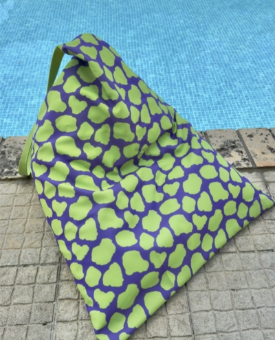 Mala saco triangular com padrão verde e roxo junto a piscina