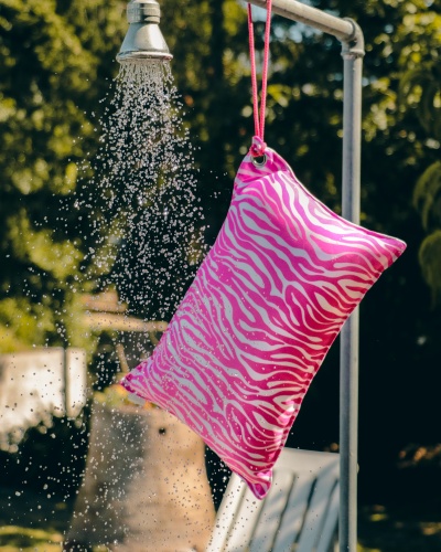 Bolsa inflável rosa com padrão de zebra pendurada perto de ducha exterior em jardim