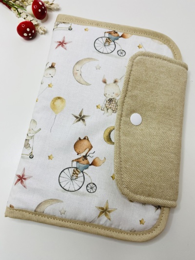 Estojo de tecido com padrão de animais e estrelas, fecho de botão branco e bordas bege, com cogumelos decorativos ao lado