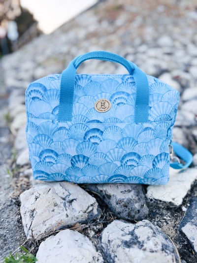Mala azul com padrão de conchas e alças azuis colocada sobre pedras brancas