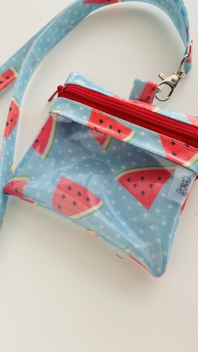 Bolsa pequena azul claro com padrão de melancias, fecho vermelho e alça com clip metálico
