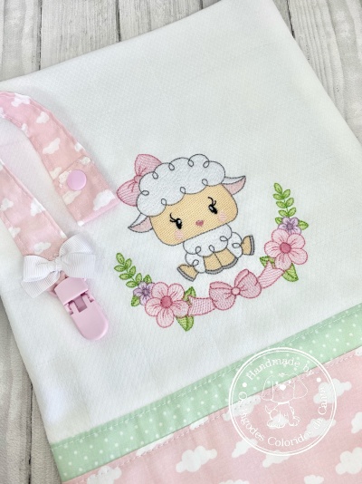 Fralda branca bordada com ovelha, flores, faixa verde e rosa, com prendedor de chupeta rosa.