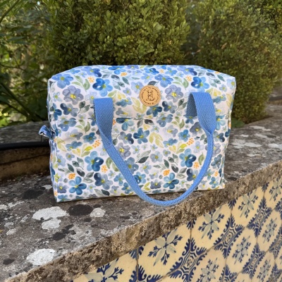 Mala de tecido floral azul com alças azuis numa superfície de pedra e azulejos azuis e brancos.