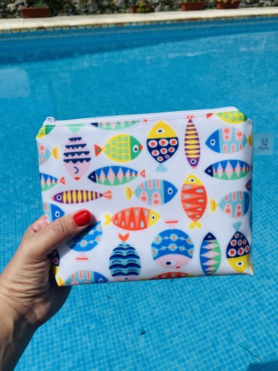 Estojo colorido com padrão de peixes segurado à frente de uma piscina