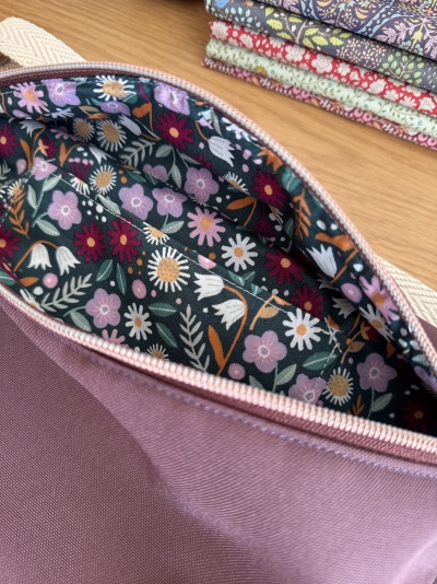 Bolsa rosa com interior floral e pilha de tecidos florais dobrados