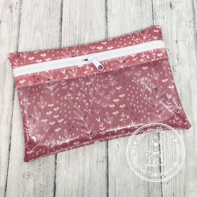 Estojo rosa com padrão de folhas e flores, com fecho branco, sobre madeira clara
