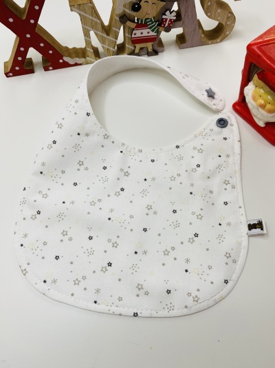 Babete branco com estrelas cinzentas e pretas e fecho azul escuro, decorado com elementos de Natal de madeira e mini Pai Natal.