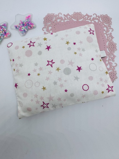 Almofada branca com padrão de estrelas e círculos coloridos sobre suporte rosa ornamental e recipientes em forma de estrela