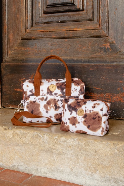 Conjunto de duas bolsas castanhas e brancas com padrão manchado, alças castanhas, num degrau de pedra e porta de madeira
