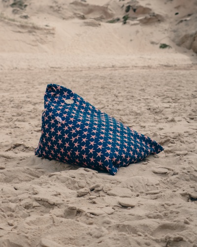 Pufe triangular azul com padrão de estrelas-do-mar cor-de-rosa na areia