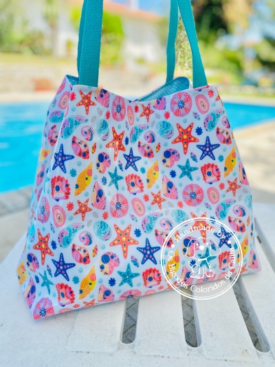 Saco de mão colorido com padrão de estrelas-do-mar e conchas e alças azuis.