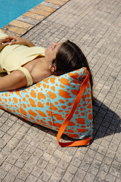 Almofada triangular azul com padrão de manchas laranjas usada ao lado de piscina