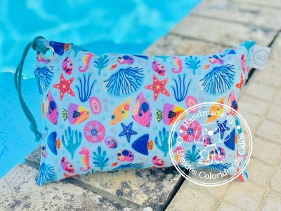 Bolsa de tecido azul com padrão marinho colorido, junto a piscina e pavimento de pedra