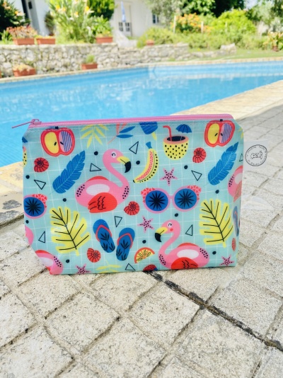 Necessaire colorida com padrão de flamingos e frutas junto a uma piscina