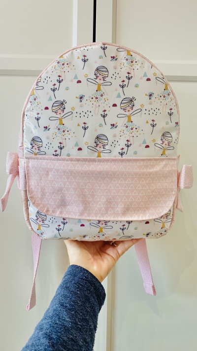 Mochila infantil branca e rosa com desenho de fadas e flores, bolso frontal rosa com triângulos brancos.