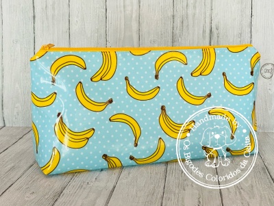 Estojo azul com padrão de bananas amarelas e fecho amarelo em superfície de madeira clara.