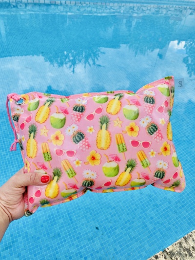 Almofada colorida com padrão tropical segurada por mão junto a piscina azul