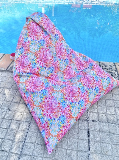 Puff triangular floral colorido ao lado de piscina