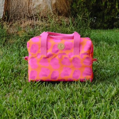 Mala cor-de-rosa com padrão alaranjado em relva e árvore ao fundo
