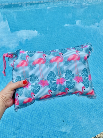 Estojo impermeável com padrão de flamingos e folhas verdes segurado diante de piscina