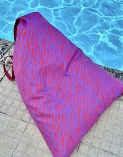 Pufe triangular com padrão zebrado laranja e violeta perto de piscina azul