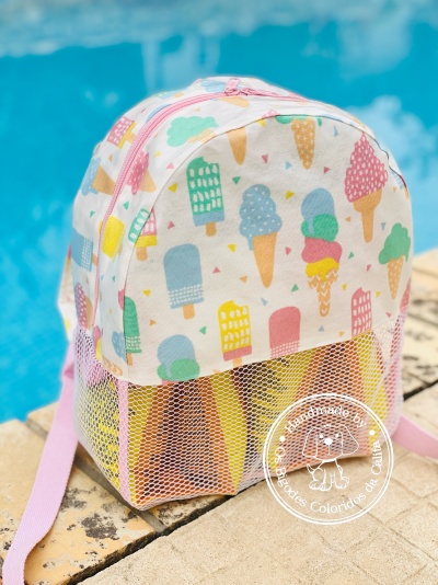 Mochila infantil colorida com padrão de gelados e picolés ao lado de uma piscina