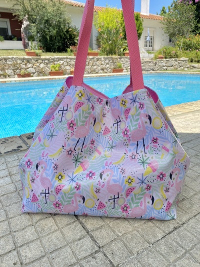 Saco de praia colorido com padrão de flamingos e alças cor-de-rosa ao lado de piscina