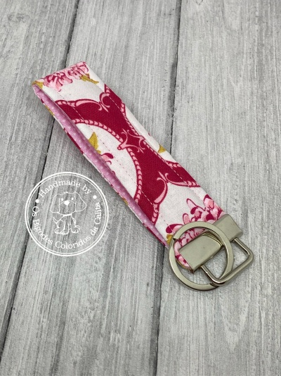 Chaveiro de tecido com padrão floral rosa e branco com argolas metálicas prateadas sobre superfície de madeira