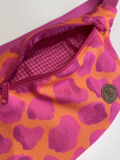 Pochete de tecido rosa e laranja com fecho e etiqueta redonda.