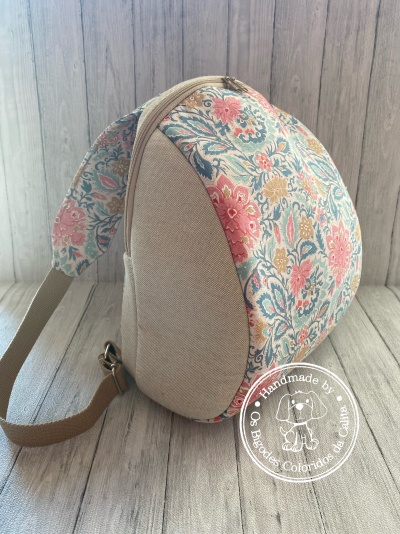 Mochila floral bege com alças castanhas sobre chão de madeira clara