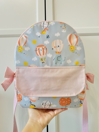 Mochila infantil com padrão de balões de ar quente e bolso frontal rosa às riscas.
