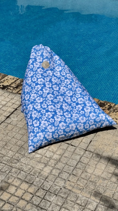Pufe triangular azul com flores brancas junto a piscina.