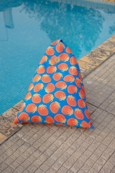 Almofada triangular azul com estampa de tomates laranja junto a piscina