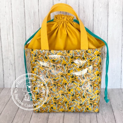 Saco tote amarelo com padrão floral e alças, fundo madeira clara