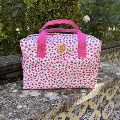 Mala floral branca com alças rosa e etiqueta Colores de Carlota, em pedra exterior com plantas