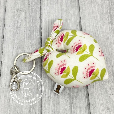 Chaveiro tecido floral branco com anel metálico prateado sobre madeira cinza