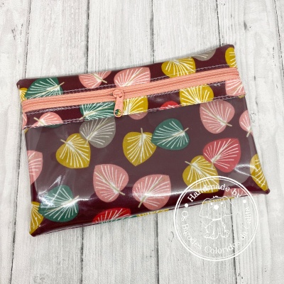 Bolsa pequena com padrão de folhas coloridas sobre fundo vinho e fecho de correr cor de rosa