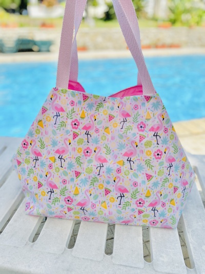 Saco de praia colorido com padrão de flamingos e flores ao lado de piscina.