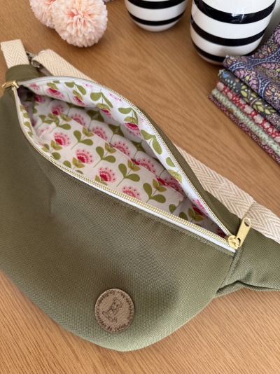 Pochete verde com fecho dourado e interior floral aberto sobre mesa de madeira
