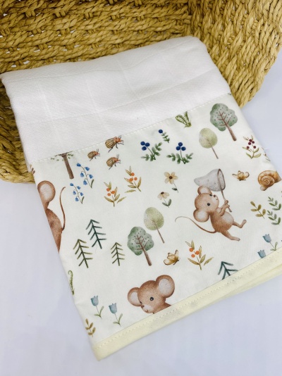 Fralda branca com padrão decorativo de ratinhos, árvores e flores coloridas colocada junto a cesto trançado