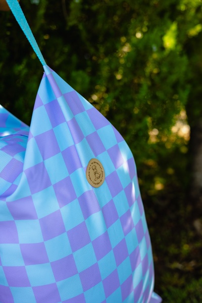 Mochila azul claro e lilás com padrão quadriculado e etiqueta redonda