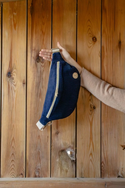 Mala de cintura azul escura com fecho dourado e alça bege contra fundo de madeira