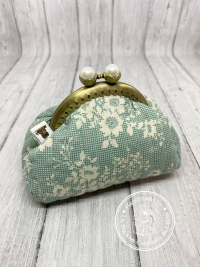 Mala pequena verde com padrão floral branco e fecho metálico dourado